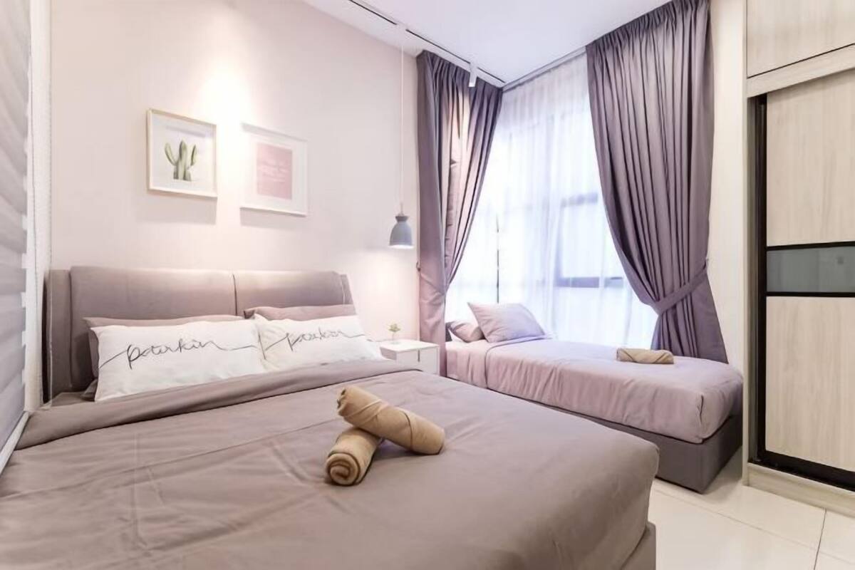 A bedroom with two beds, a nightstand, a lamp, and a window with curtains.