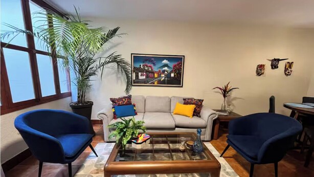 A living room with a sofa, two armchairs, a coffee table, a large potted plant, and a painting on the wall. - Excellent location in Antigua for 4 guests (Antigua Guatemala)