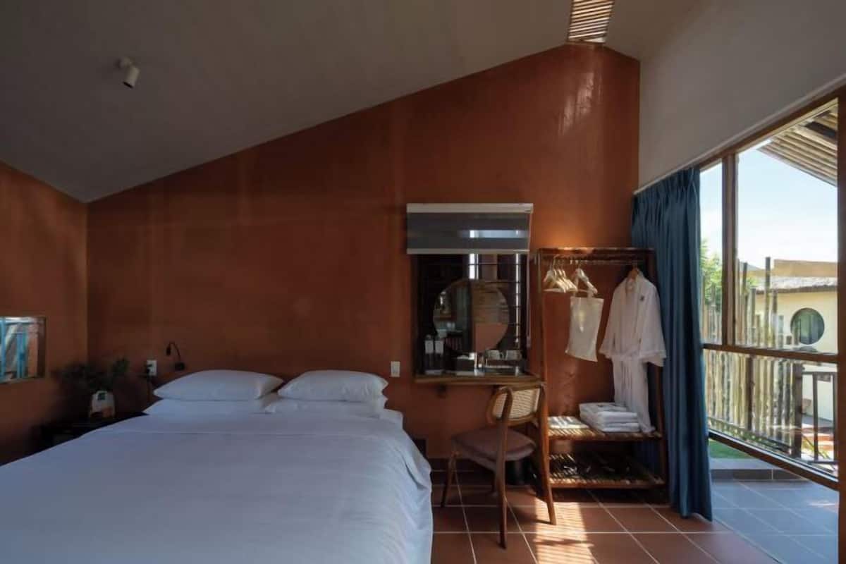 A bedroom with a bed, a chair, a desk with a mirror, and a window with curtains.