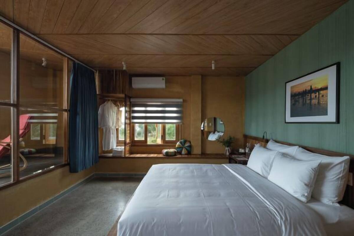A bedroom with a large bed, a window with blinds, a mirror, and a painting on the wall.
