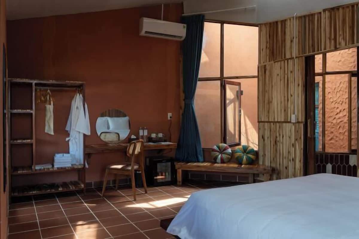 A room with a bed, a desk, a chair, a shelf with clothes, and a window with curtains.