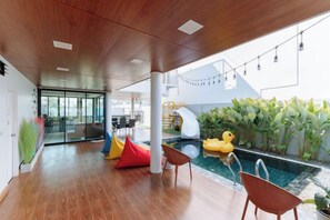 Un espace piscine intérieur moderne avec un plafond en bois, des sièges colorés et un petit canard gonflable.