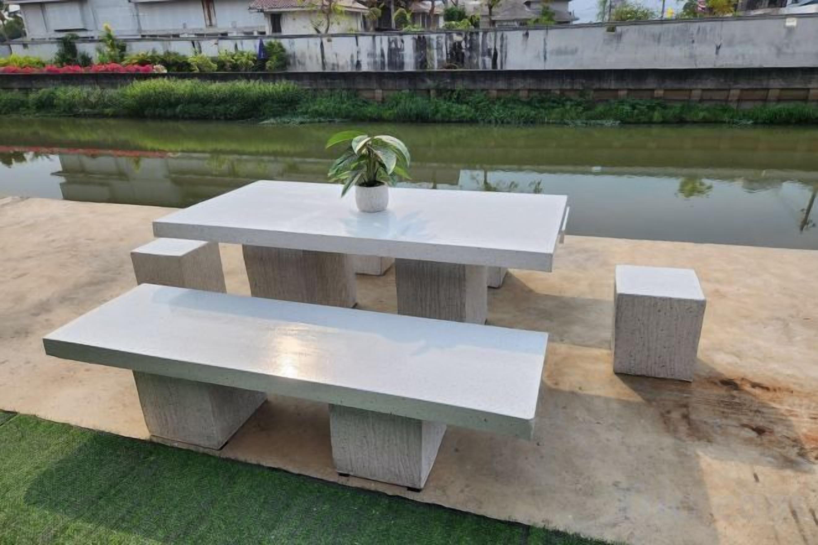 Un área de estar exterior de concreto con bancos y una mesa, cerca de una masa de agua.