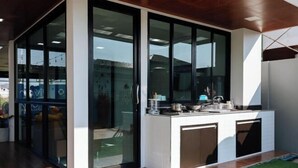 A modern kitchen with a glass door, a built-in stove, and a small island. - Riverfront Pool Villa Rangsit Klong 4 (Thanyaburi)