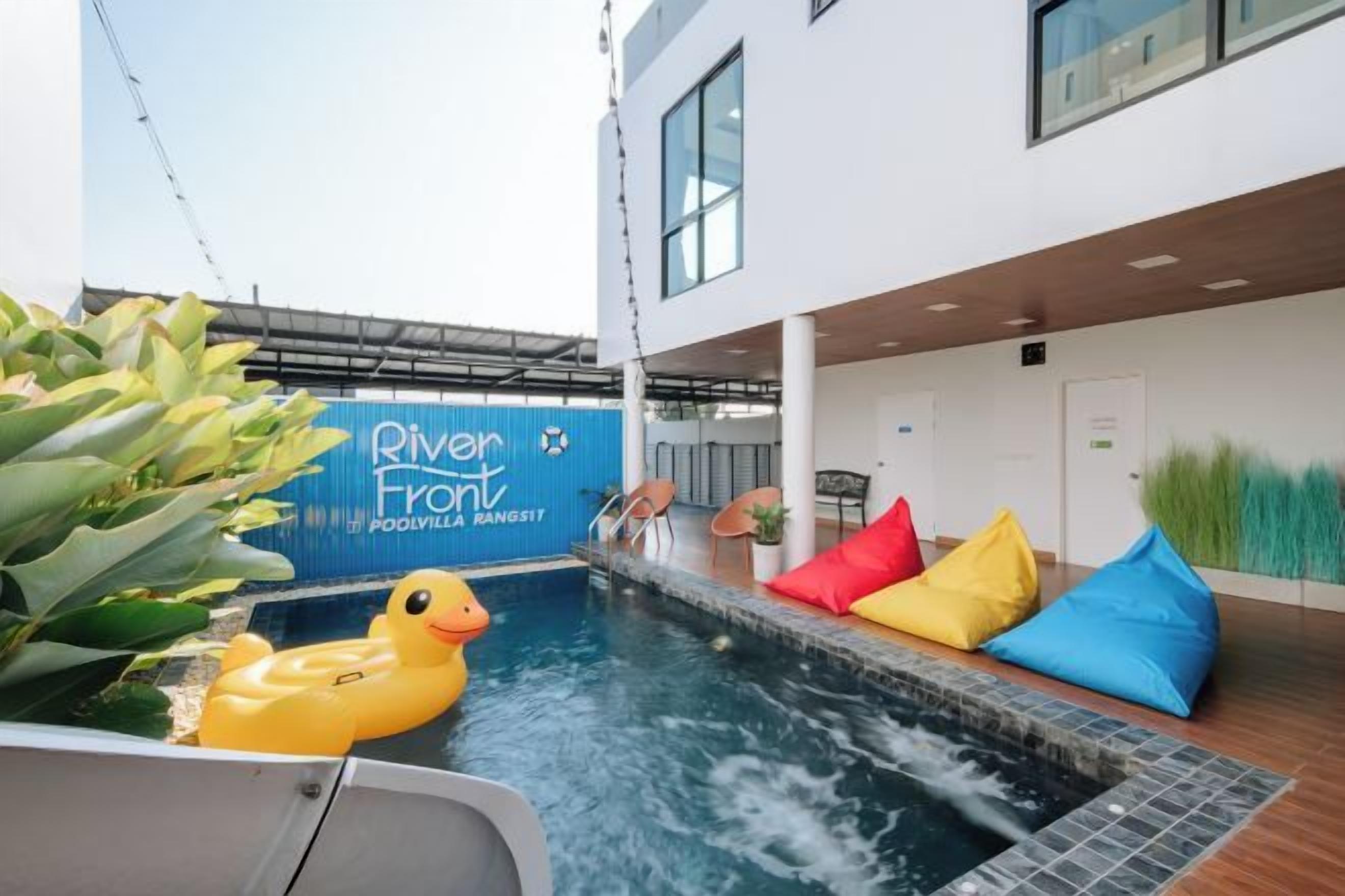Interior moderno de un hotel con piscina, cojines de colores y un cartel que dice 'River Front'.
