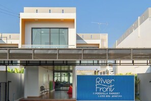 A modern building with a covered walkway, a sign for Riverfront POPOVILLA RANGSIT, and a clear sky.