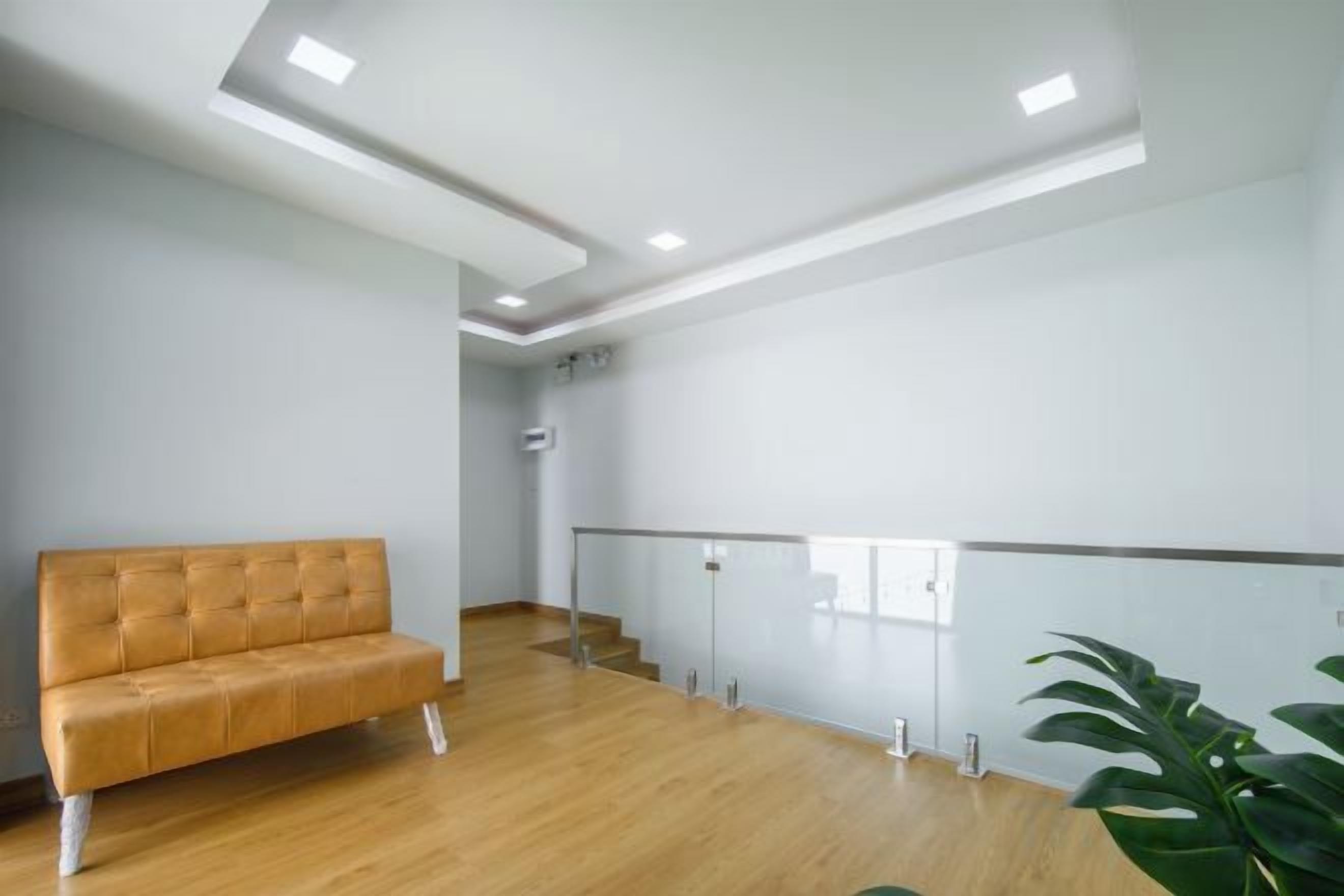 Una habitación con piso de madera, un sofá, una escalera y una planta.