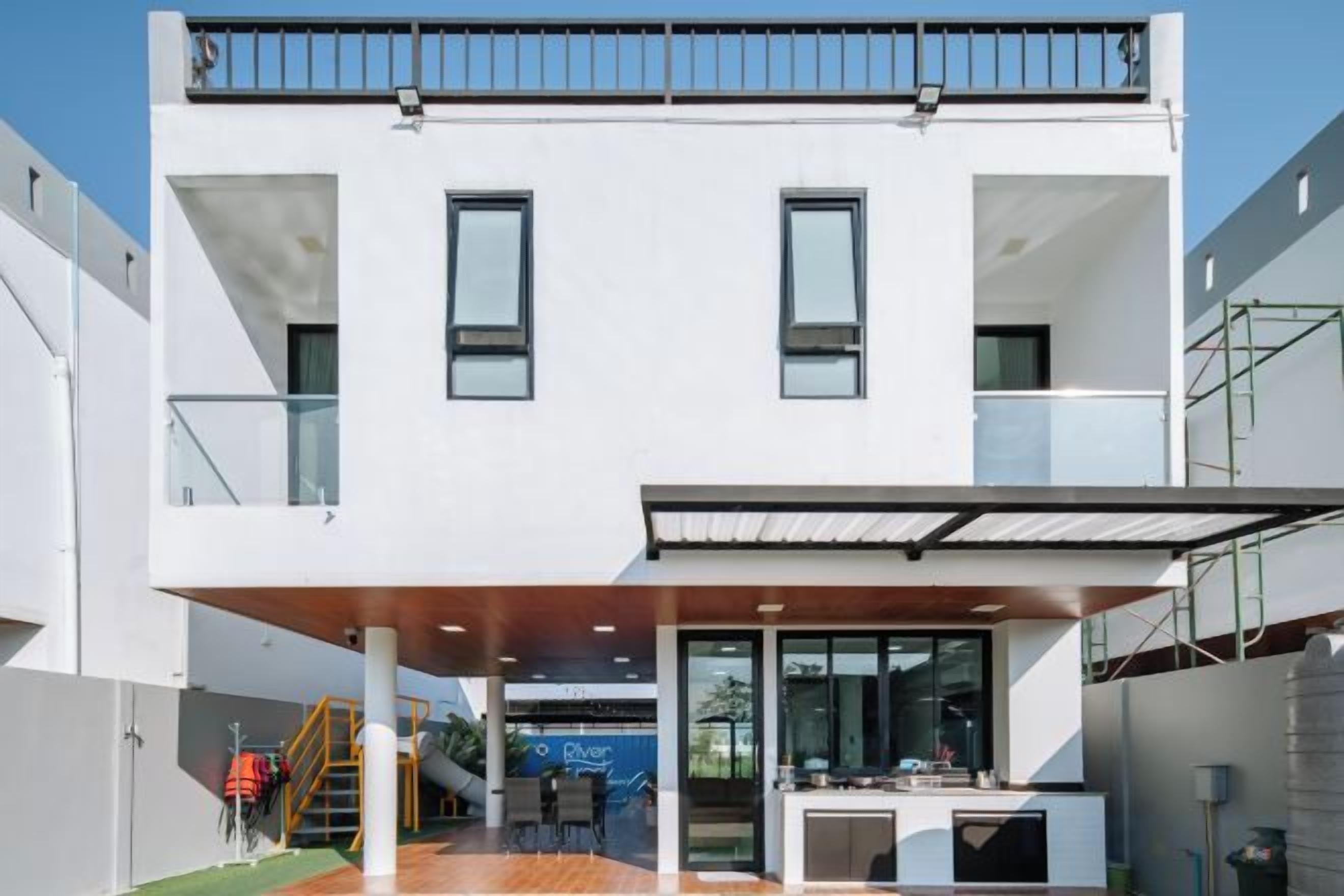 Un edificio moderno de dos pisos con techo plano, ventanas grandes y un espacio exterior cubierto con disposición de asientos.