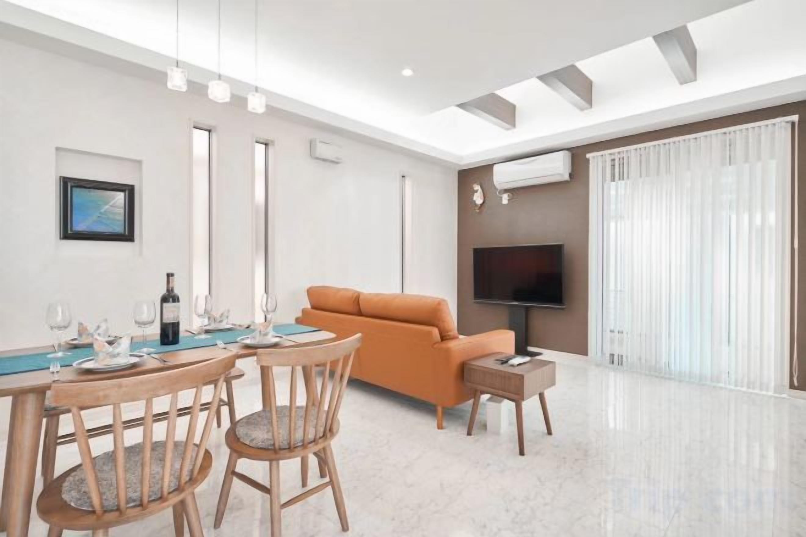Una sala moderna con comedor, un sofá, un televisor de pantalla plana y un amplio ventanal con cortinas.