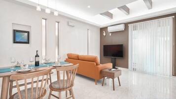 Una sala moderna con comedor, un sofá, un televisor de pantalla plana y un amplio ventanal con cortinas.