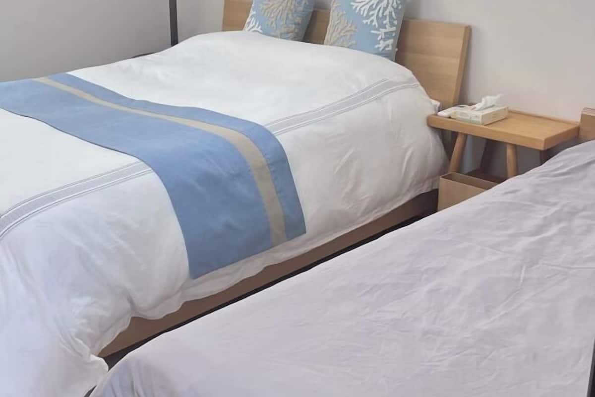 A hotel room with two beds, a bedside table with a phone, and a nightstand with a lamp.