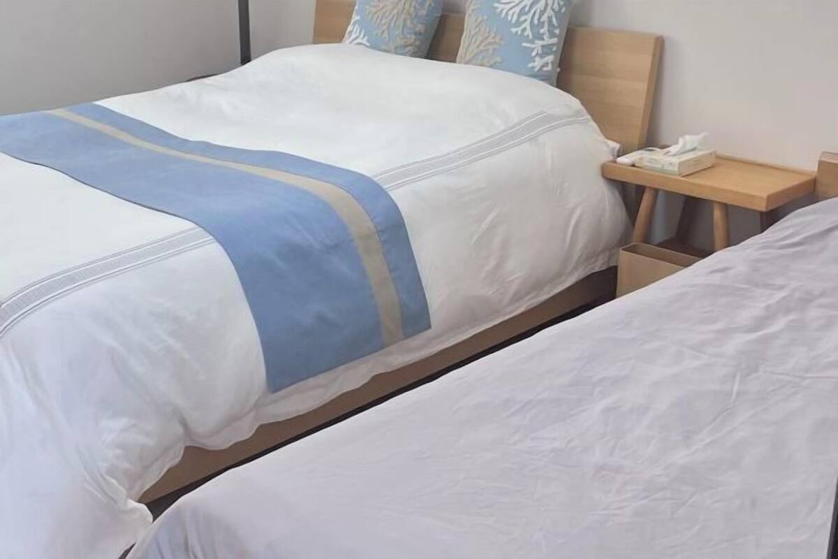 A hotel room with two beds, a bedside table with a phone, and a nightstand with a lamp.