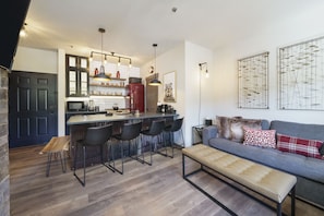 A modern kitchen with a central island, bar stools, and a seating area with a sofa and bench.