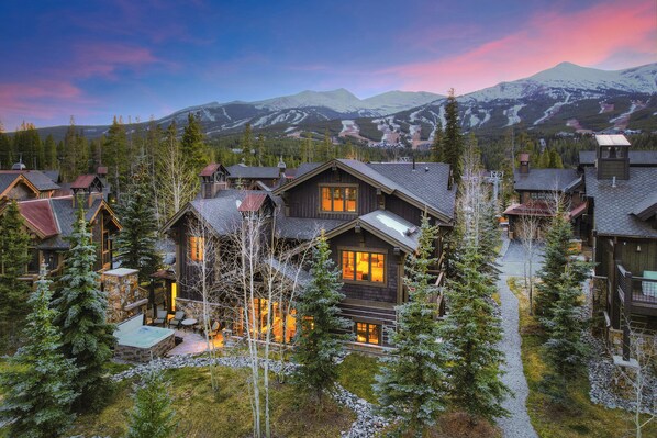 Un chalet avec une façade en pierre, une terrasse en bois et une vue sur des montagnes enneigées.