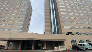 A multi-story hotel with a prominent entrance, a parking area with cars, and a clear sky.