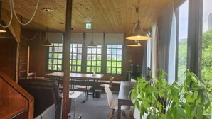 A wooden interior with tables and chairs, large windows, and hanging lights. - Lodge noel (Minamiuonuma)
