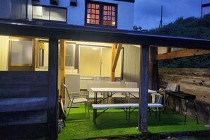 An outdoor dining area with tables and chairs, a wooden fence, and a building with windows in the background. - Lodge noel (Minamiuonuma)