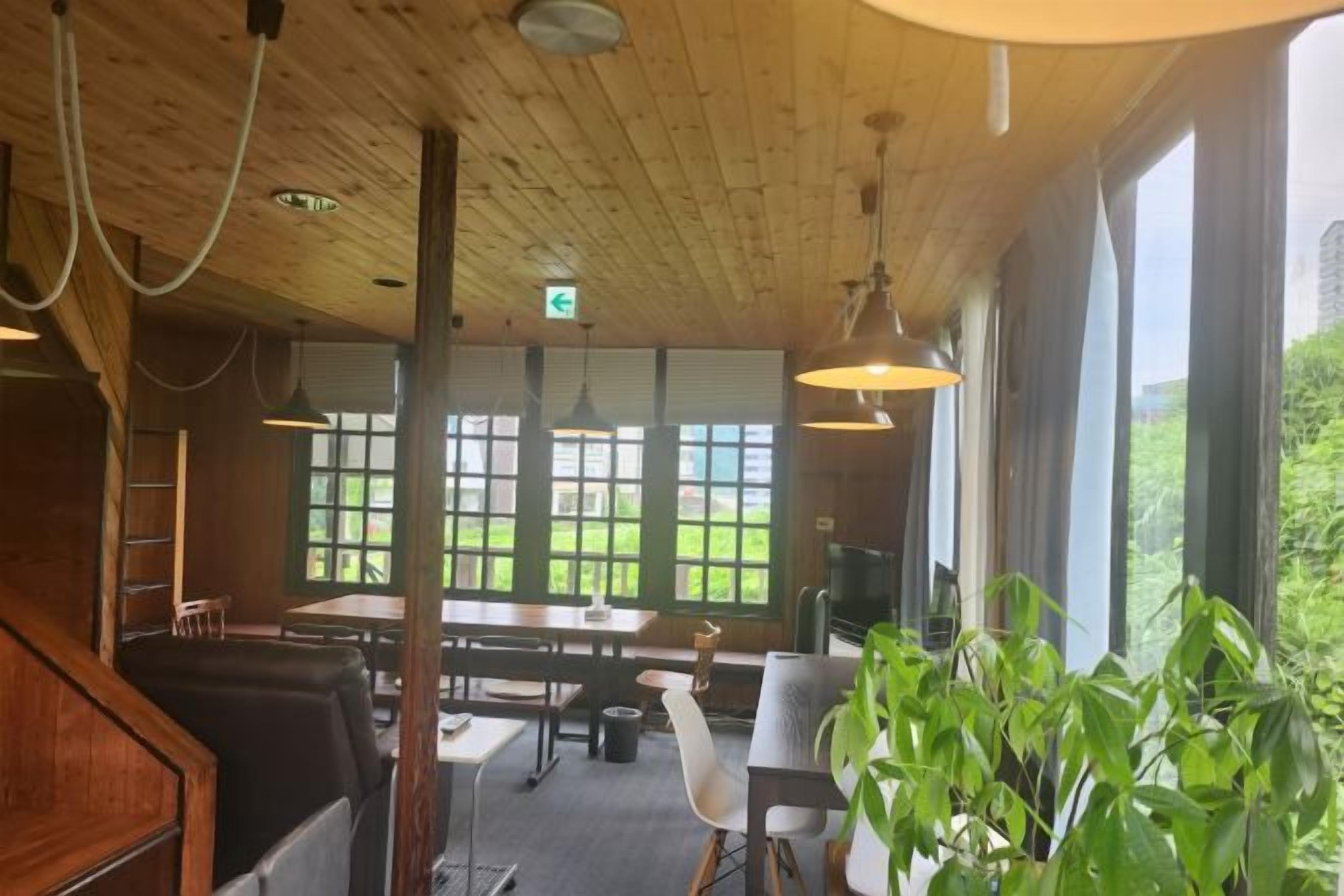 Een houten interieur met tafels en stoelen, grote ramen en hanglampen.