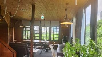 Een houten interieur met tafels en stoelen, grote ramen en hanglampen.