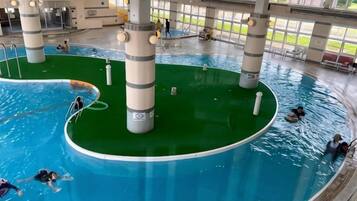 En inomhuspool med flera banor, ett centralt grönområde och folk som simmar och leker.