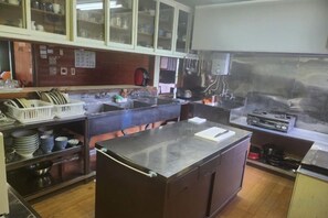 A commercial kitchen with stainless steel appliances, a large central island, and a window overlooking the kitchen area. - Lodge noel (Minamiuonuma)