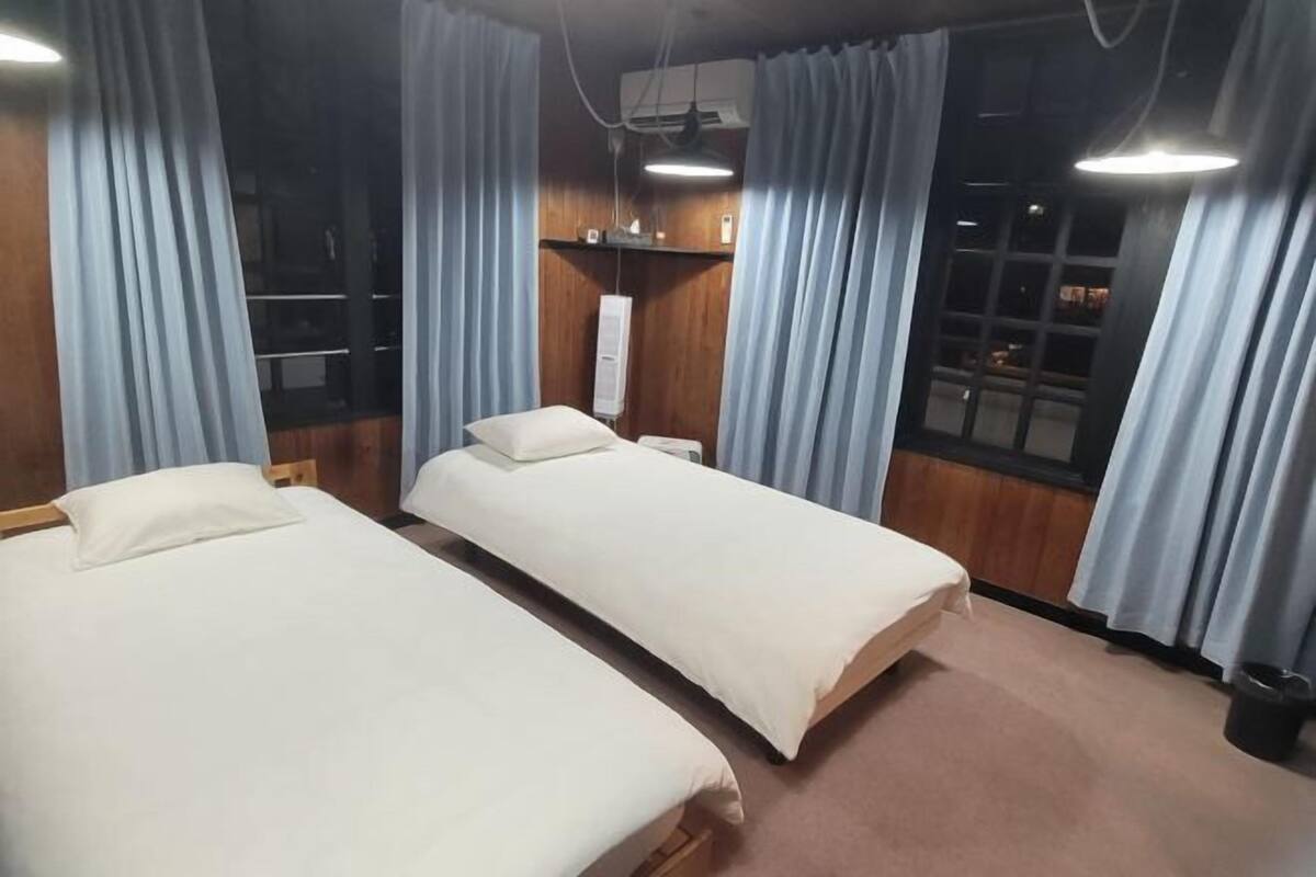 A room with two beds, a wooden wardrobe, a mirror, and a window with curtains.