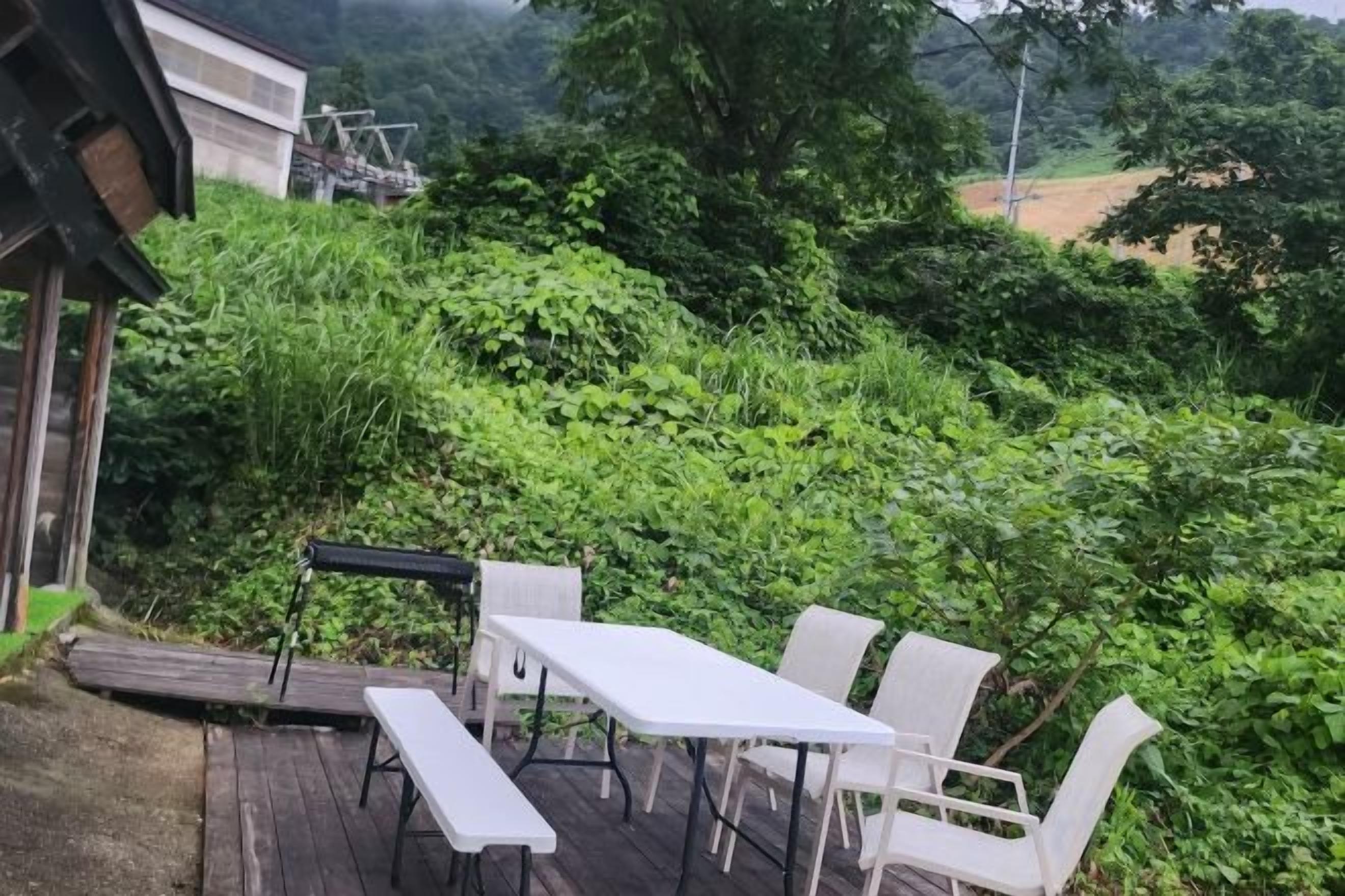 An outdoor patio with a table and chairs, surrounded by lush greenery.