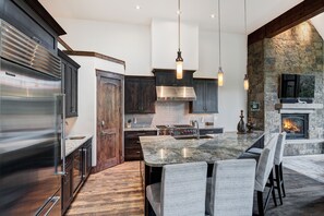 A modern kitchen with a large island, dark wood cabinets, stainless steel appliances, and a stone fireplace.