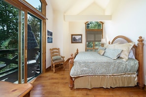 Une chambre avec un grand lit, une chaise en bois, une petite table et une fenêtre donnant sur un balcon.