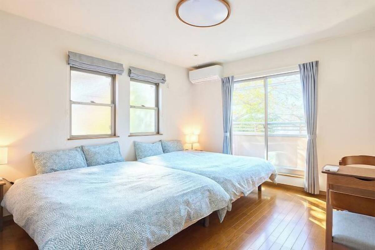 A bedroom with two beds, a wooden floor, and a window with curtains.