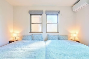 A room with two beds, two windows with curtains, bedside lamps, and an air conditioning unit. - Ueno Nippori Terrace Kando (Tokyo)