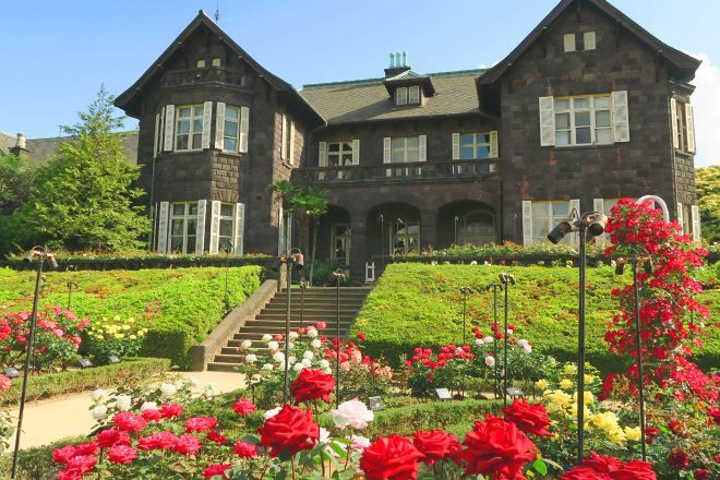 A large stone building with a symmetrical facade, a central entrance with steps, and a well-maintained garden with various flowers.