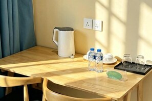 A wooden table with a kettle, water bottles, cups, and glasses, a power outlet, and a small green sign. - ZHIYUANTA HOTEL (Vientiane)