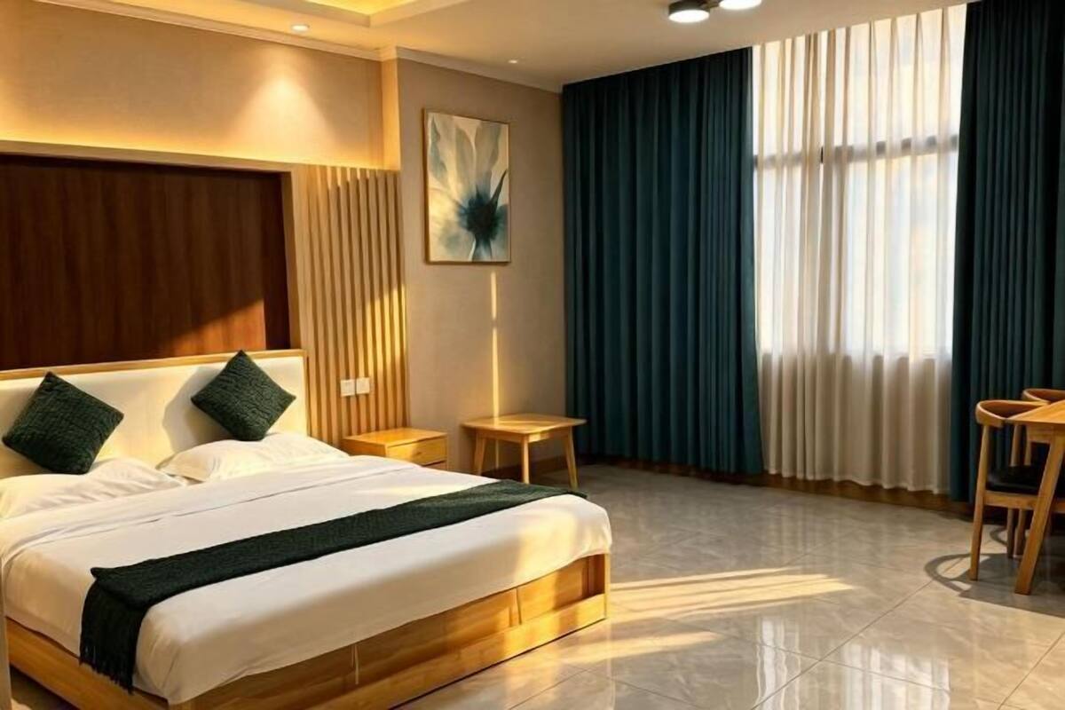 A hotel room with a bed, a bedside table, a chair, a window with curtains, and a wall-mounted artwork.