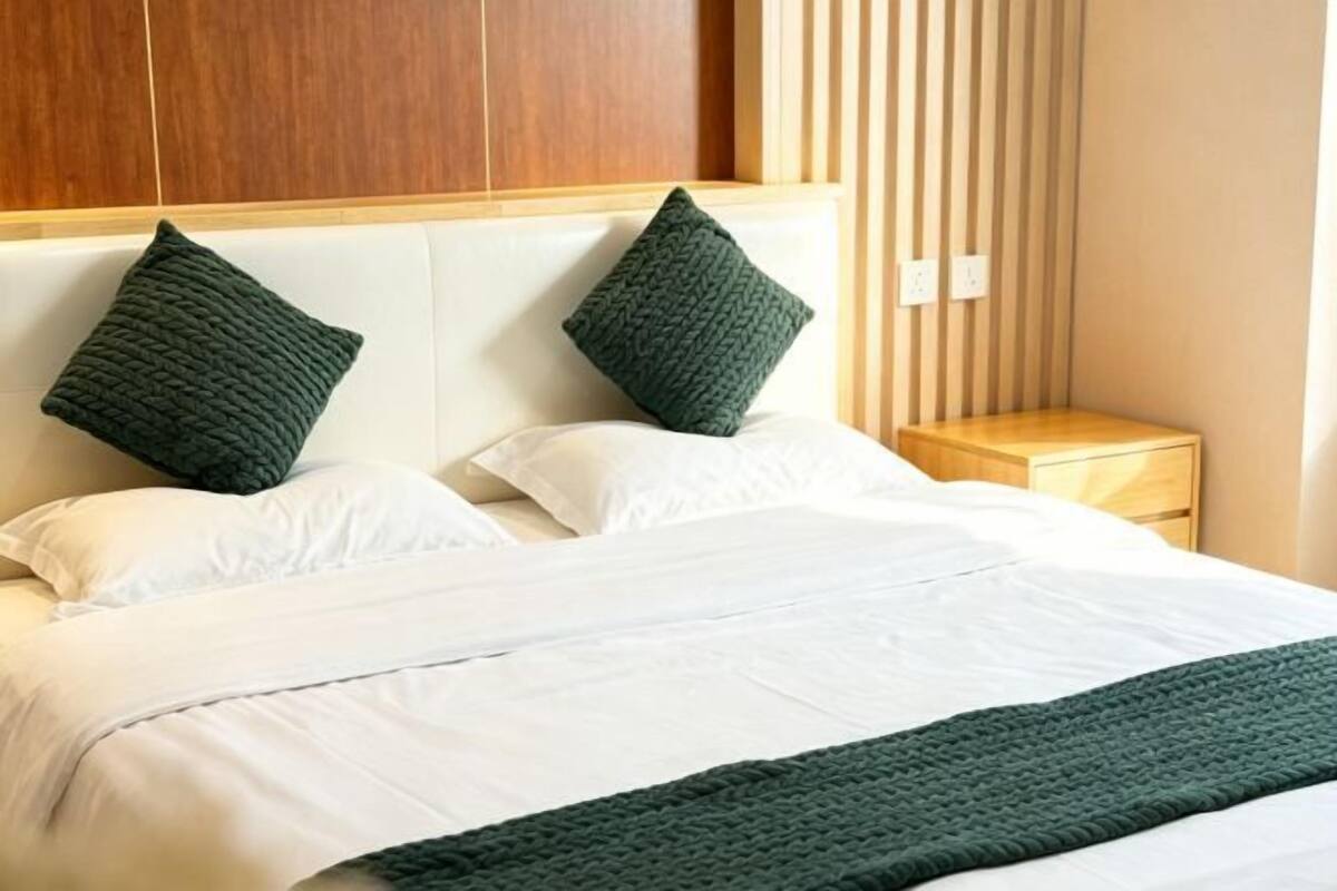 A bed with white linens, two dark green pillows, and a matching green throw blanket.