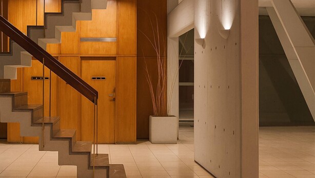 Ein modernes Interieur mit einer Holztreppe, einer weißen Wand mit geometrischem Muster und einem Blumentopf.