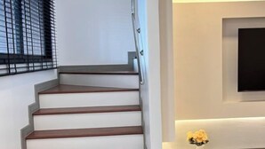 A staircase with wooden steps and a metal handrail, leading to a landing with a flat surface and a wall-mounted television. - Pattaya Tay Emperor Holiday townhouse (Pattaya)