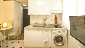 A compact kitchen with white cabinets, a built-in washing machine, a sink, and a small dining area with a table and chairs. - CareCove (Seoul)
