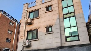 A multi-story building with a beige facade, large windows, and air conditioning units. - CareCove (Seoul)