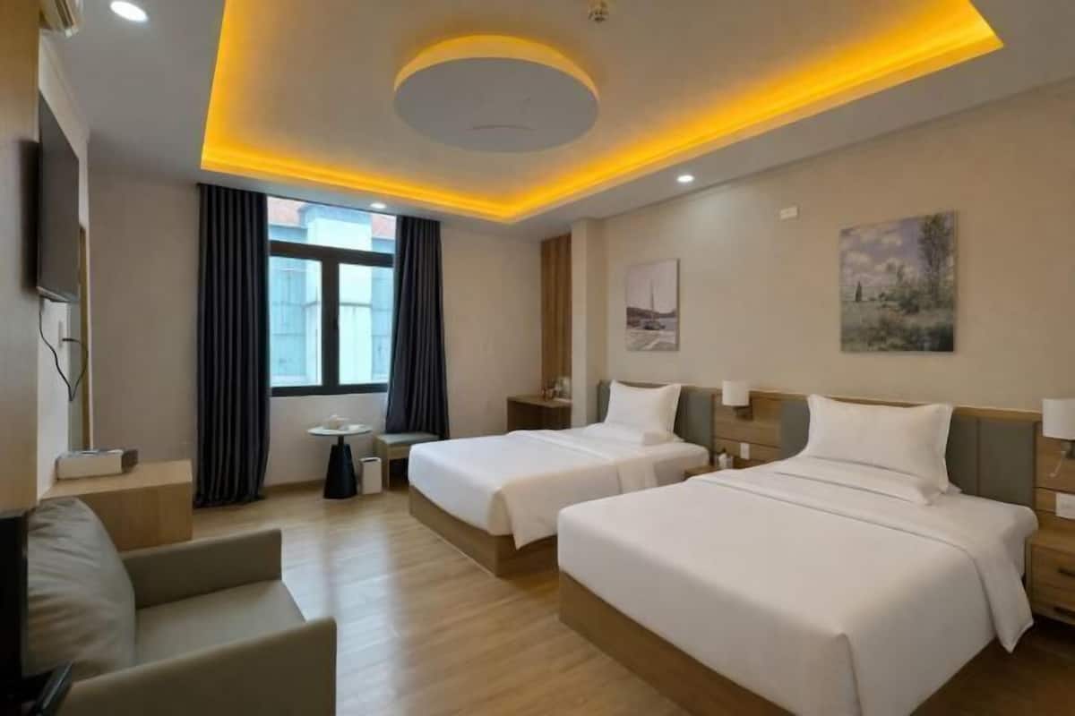 Une chambre d’hôtel avec deux lits, un canapé, une petite table et un luminaire au plafond.