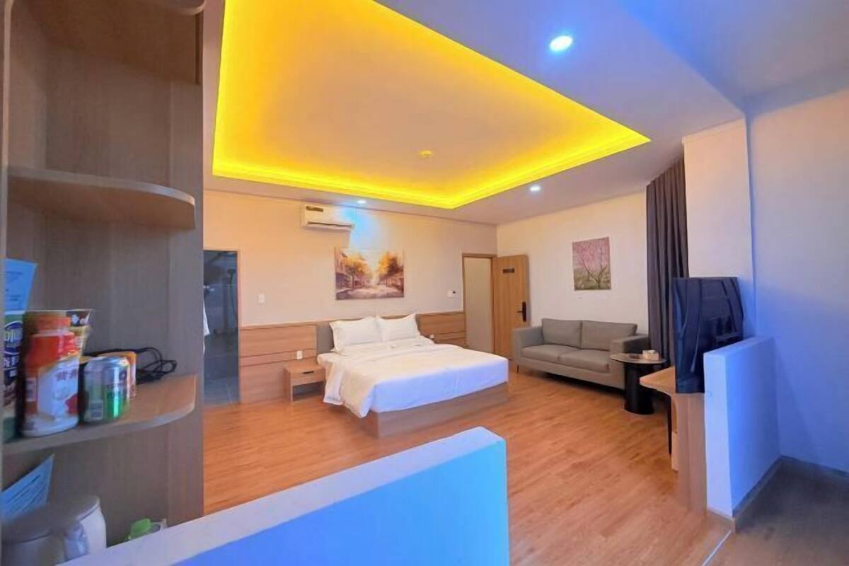 Une chambre d’hôtel moderne équipée d’un lit, d’un canapé, d’une petite table et d’une étagère avec quelques objets.