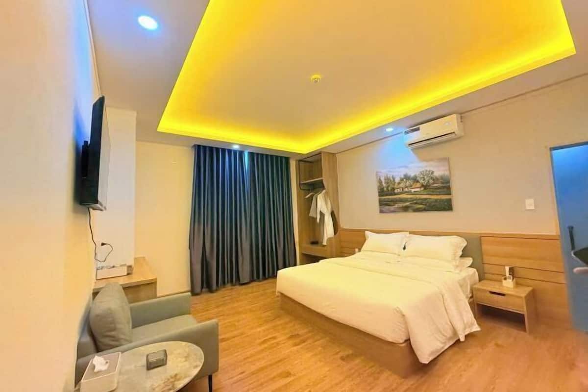 Une chambre d’hôtel avec un lit, un bureau, une chaise, une petite table, un téléviseur fixé au mur et un tableau accroché au mur.