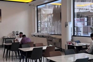 Un comedor con mesas y sillas, un amplio ventanal con vista a la calle y una pantalla de proyección mostrando una imagen.