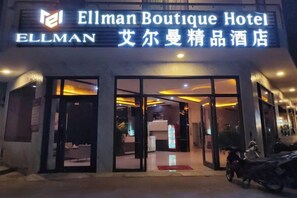 Exterior del Hotel Ellman Boutique, con entrada despejada, mostrador de recepción y una motocicleta estacionada afuera.