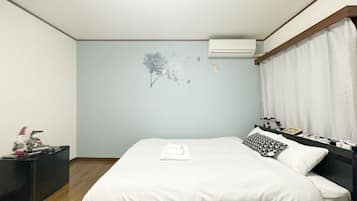 A bedroom with a bed, a nightstand, a wall-mounted air conditioner, and a window with curtains.