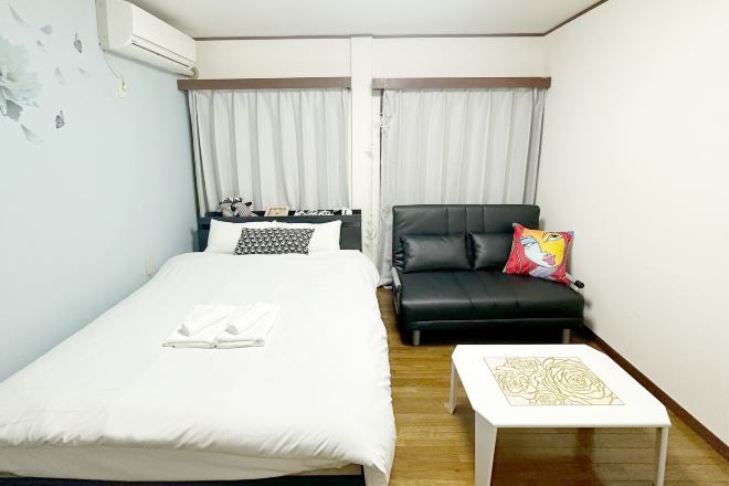 A hotel room with a bed, a black leather sofa, a small white table, and a window with curtains.