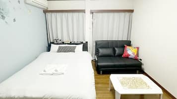 A hotel room with a bed, a black leather sofa, a small white table, and a window with curtains.