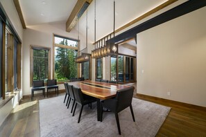 A modern dining area with a long wooden table, black chairs, and pendant lighting.