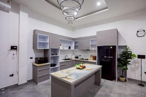 A modern kitchen with built-in shelves, a central island, and a refrigerator. - THE I-CON Luxury PoolVilla Pattaya "10 bed" Ocean Yacht Club 4 km (Pattaya)