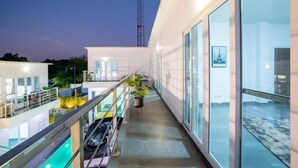 Een modern gebouw met een glazen gevel, een balkon met een auto, en een zwembad.
